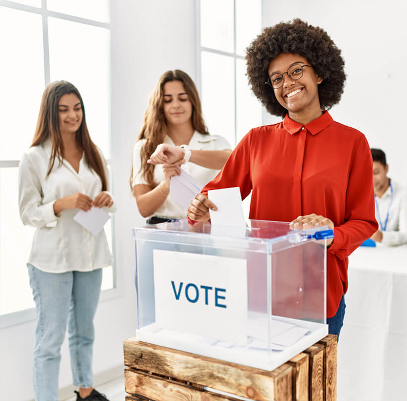 A woman places her vote into a ballot box, representing the democratic process and the importance of voting.
